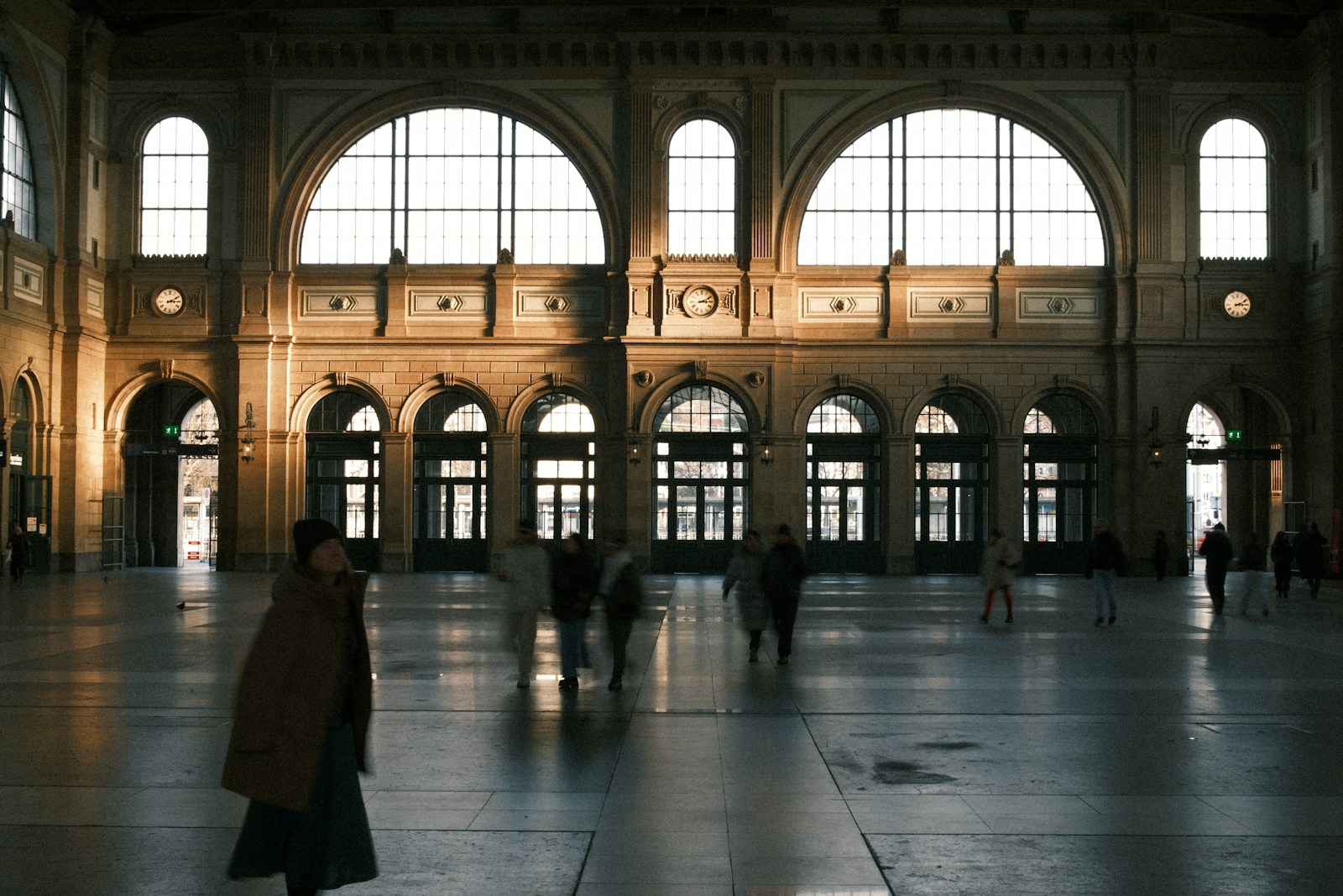 People walking through a grand, sunlit train station hall.