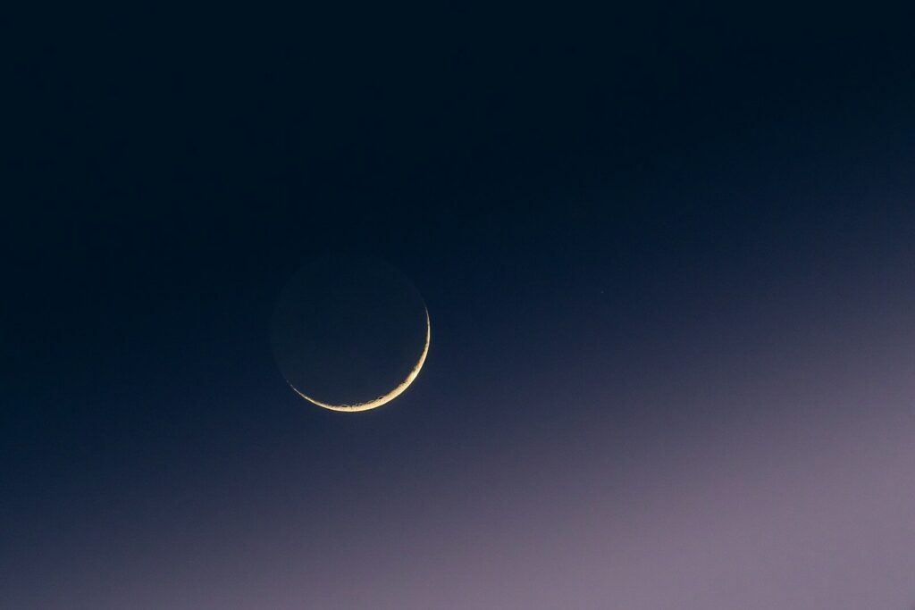 Crescent moon in a dark, gradient sky.