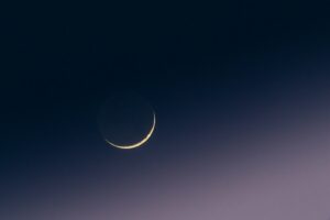 Crescent moon in a dark, gradient sky.