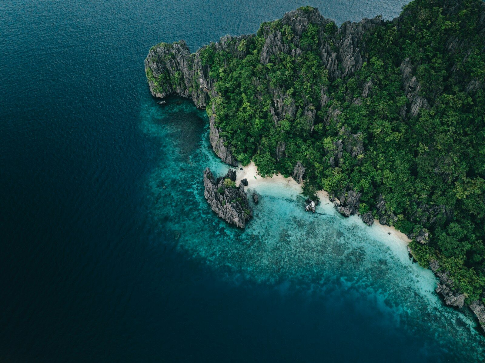 Lush green island with rocky cliffs and white sand beach.